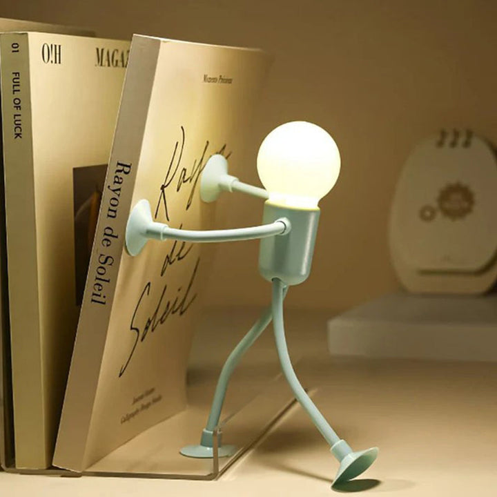 Grünes Männchen-Licht stemmt sich mit beiden Saugnapf-Händen gegen ein Buch, das an anderen Büchern lehnt, und leuchtet warm. 9