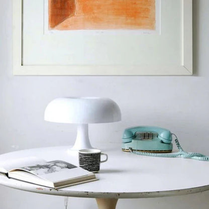 Weiße Tischlampe, Retro-Telefon, Kaffeetasse auf rundem Tisch vor Kunstwerk an weißer Wand.