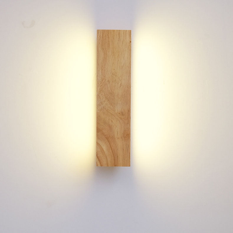 Frontansicht der senkrecht montierten Holzlampe, das Licht strahlt warm nach links und rechts an die Wand. 3