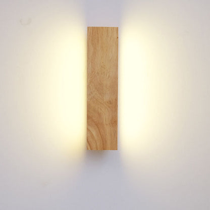 Frontansicht der senkrecht montierten Holzlampe, das Licht strahlt warm nach links und rechts an die Wand. 3