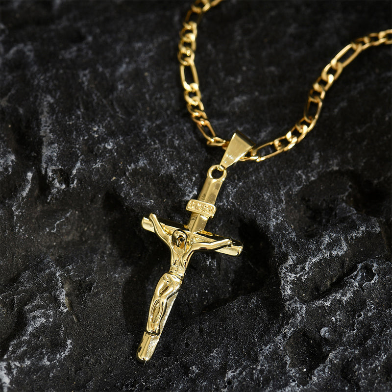 Goldfarbener Kruzifix-Anhänger mit Figarokette liegt auf dunklem, grau gemasertem Stein 9