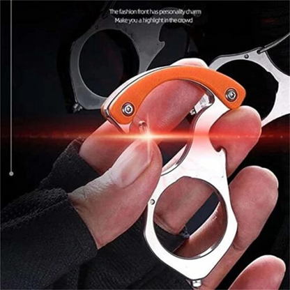 Hand hält den silbernen Karabiner mit orangem Griff und Fingerloch vor dunklem Hintergrund, im Hintergrund weitere Exemplare. 1