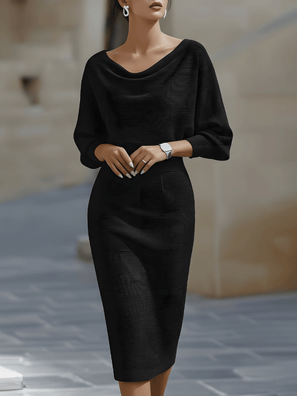 Frontansicht: Model in schwarzem, fein gerippt gestricktem Midikleid mit Wasserfallausschnitt, weiten Fledermausärmeln und enger Taille, im Freien. 1