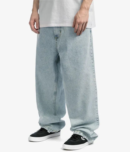 Mann trägt weite, hellblaue Jeans und schwarze Sneaker, lässiger Streetwear-Look.