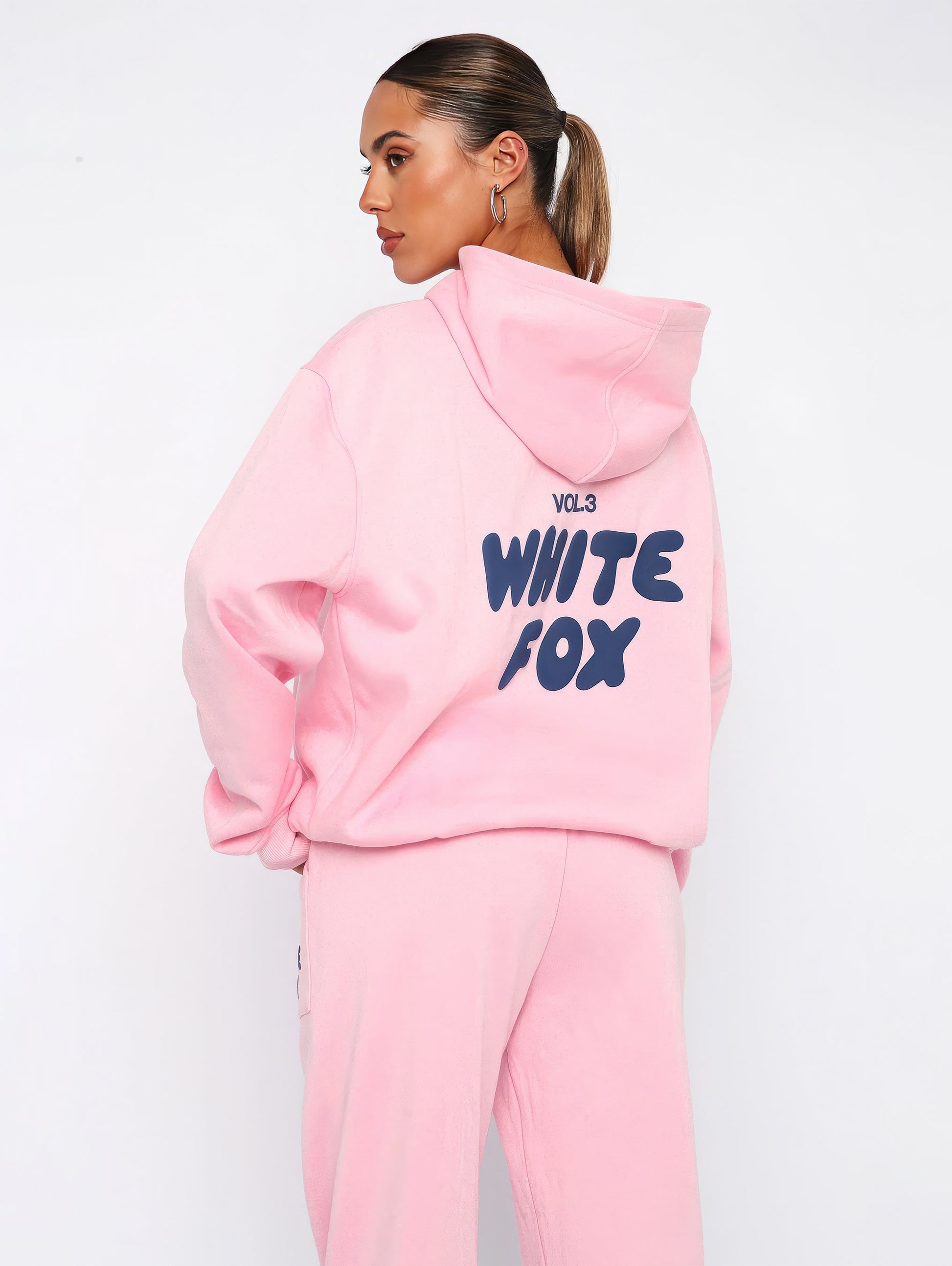 Frau in rosa Hoodie und Jogginghose mit "White Fox" Aufdruck, sportliche Damenmode.