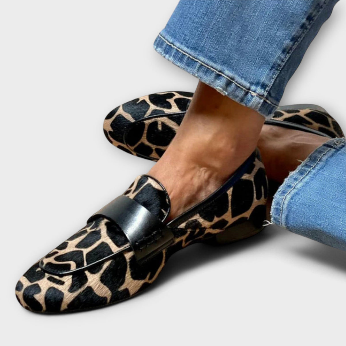 Nahaufnahme der Loafer an den Füßen mit Jeans, Blick auf das Fellmuster, die schwarze Lederspange und die flache Sohle. 2