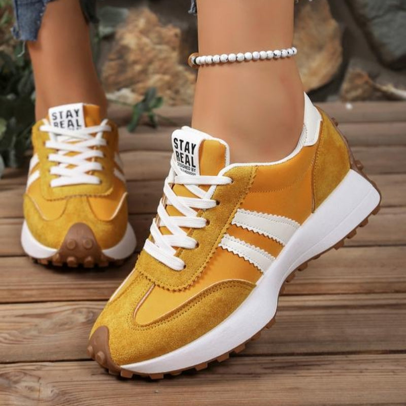 Gelbe Sneaker mit weißen Streifen und Schnürung, getragen auf Holzdielen, Nahaufnahme von der Seite 6