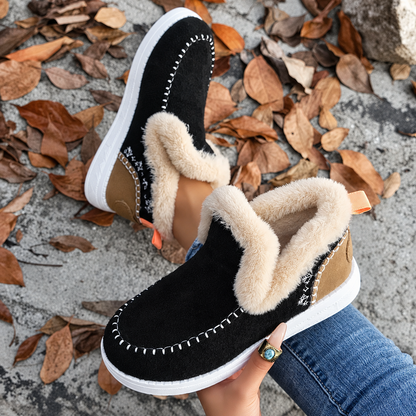 Schwarze Slip-On-Sneaker mit Plüschkragen, brauner Fersenpartie und orangefarbener Schlaufe, Draufsicht aus Schrägperspektive auf Herbstlaub. 7