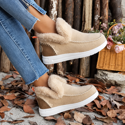 Beige Slip-On-Sneaker in Veloursoptik mit Plüschkragen und weißer Sohle, von einer Frau in Jeans seitlich getragen. 3
