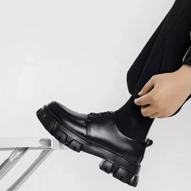Schwarzer Lederschuh mit dicker Sohle, Herrenmode, elegantes Design, auf Leiter.