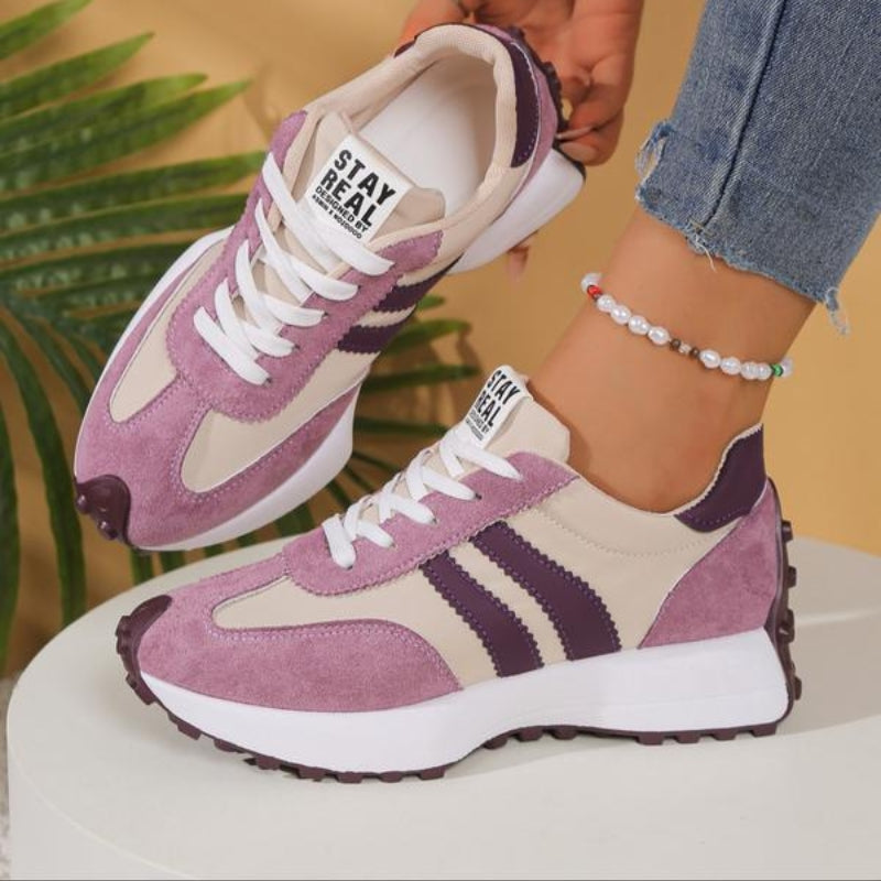 Flieder-beige Sneaker mit dunkelvioletten Streifen, einer angehoben, getragen vor Palmenblatt und Podest 11