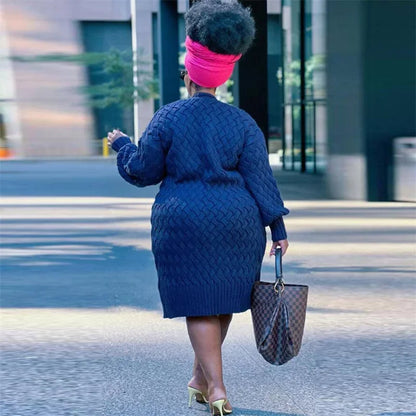 Frau in blauem Strickkleid mit pinkem Turban und brauner Tasche auf städtischer Straße.