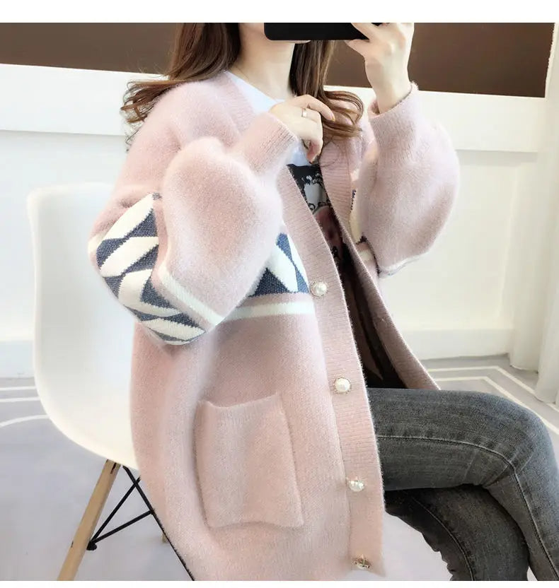 Frau in rosa Strickjacke mit geometrischem Muster, sitzt auf weißem Stuhl, modisch, gemütlich.