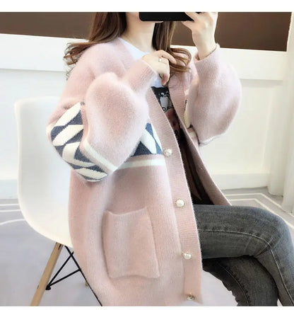 Frau in rosa Strickjacke mit geometrischem Muster, sitzt auf weißem Stuhl, modisch, gemütlich.
