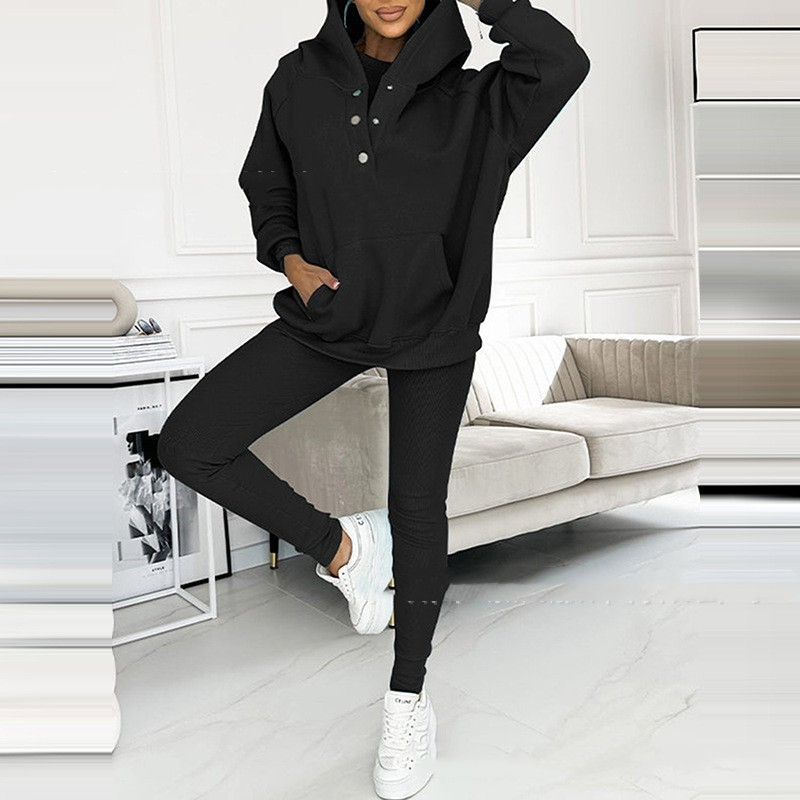 Frau in schwarzem Hoodie und Leggings, weiße Sneaker, modernes Wohnzimmer, Freizeitmode.