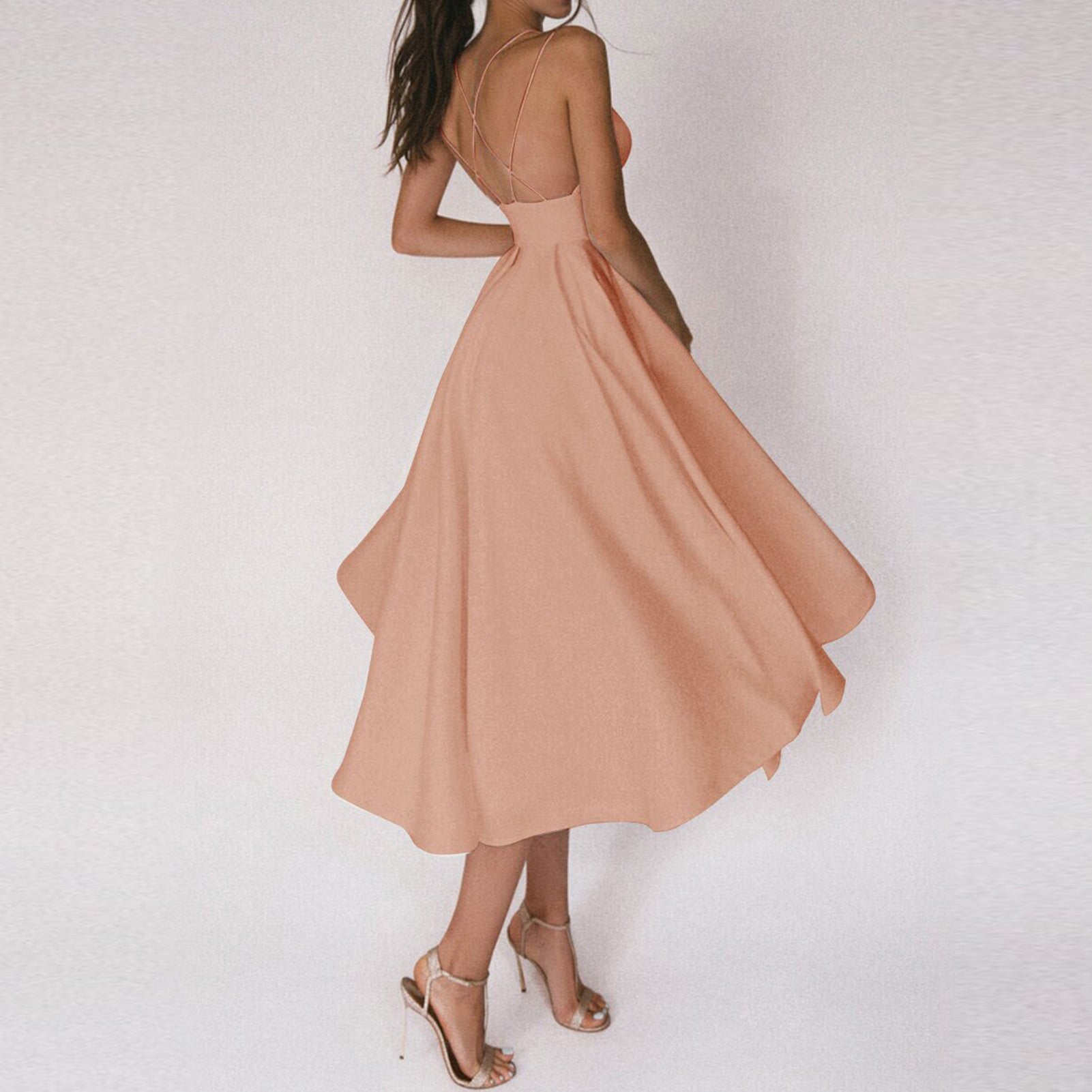 Frau in elegantem, pfirsichfarbenem Sommerkleid mit Spaghettiträgern und Sandaletten.