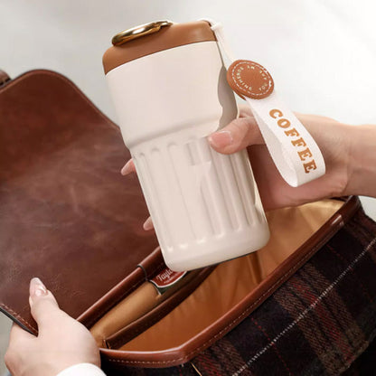 Beiger Thermobecher mit braunem Deckel und COFFEE-Schriftzug, ideal für unterwegs.