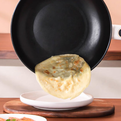 Schwarze Bratpfanne mit weißem Griff, Pfannkuchen wird auf weißen Teller serviert.