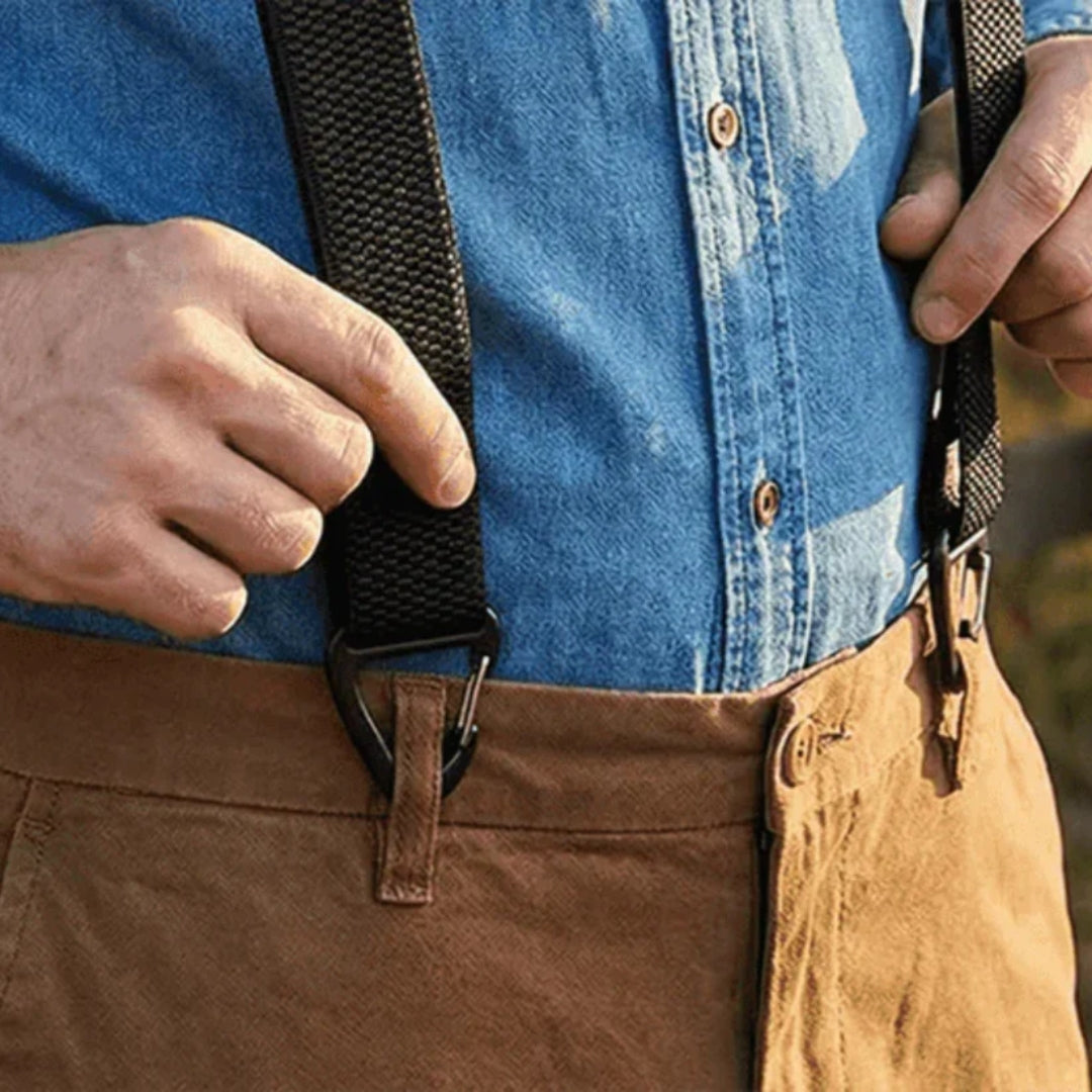 Nahaufnahme: Klammer eines schwarzen Hosenträgers am Hosenbund einer braunen Hose, darüber ein Jeanshemd 17