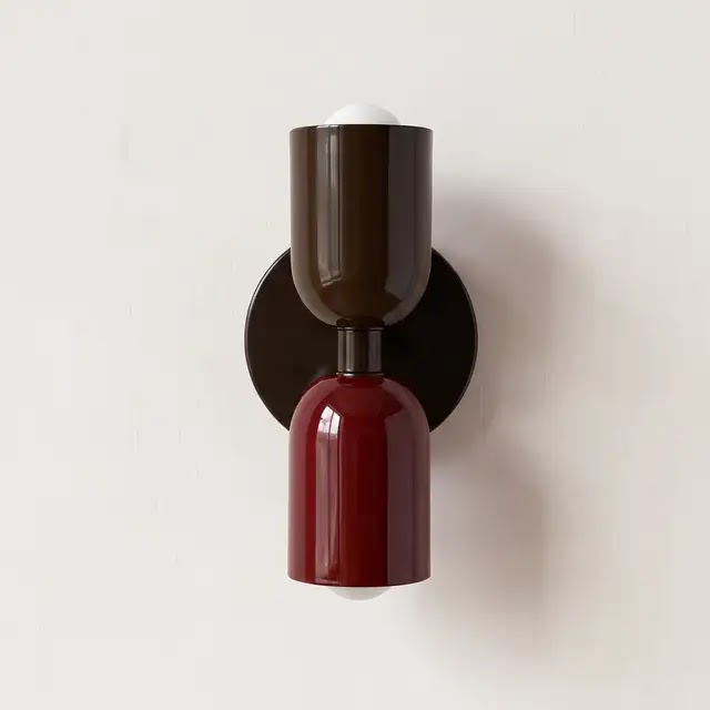 Wandleuchte mit braunem oberem und dunkelrotem unterem Schirm an einer runden dunklen Wandplatte, glänzende Lackoberfläche vor heller Wand. 24