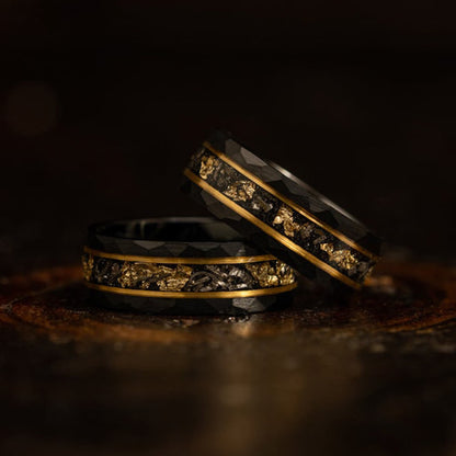 Zwei schwarze Wolframringe mit goldenen Akzenten und facettiertem Design auf dunklem Hintergrund.