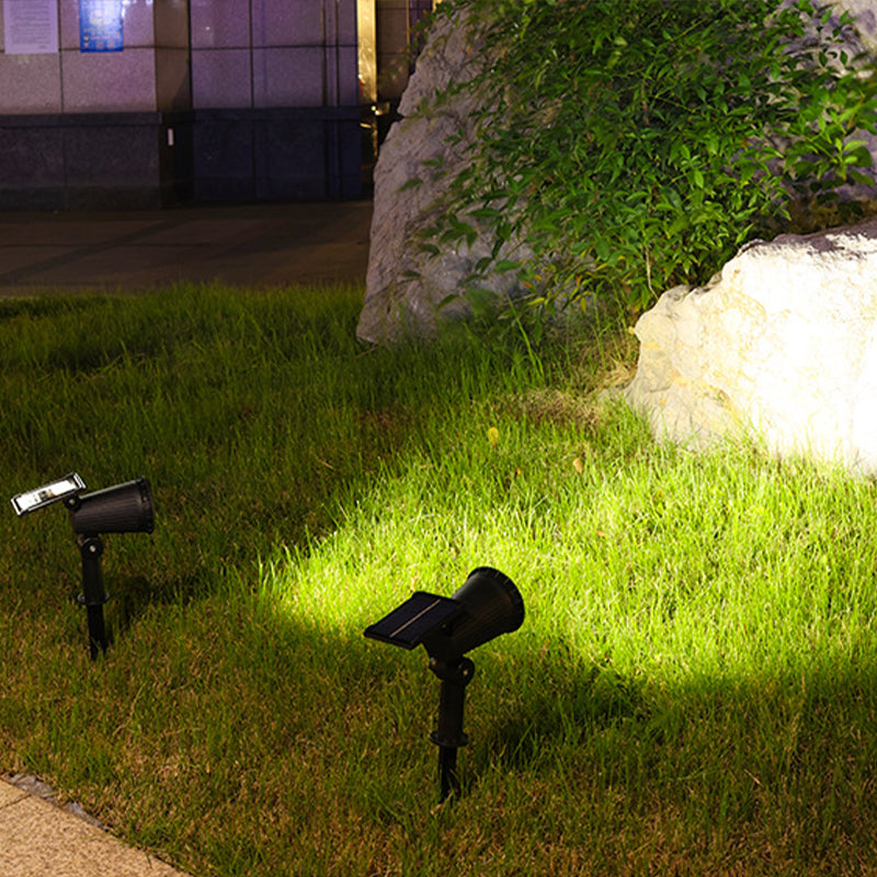 Schwarze Solar-Gartenleuchten beleuchten Rasen vor Stein und Pflanzen bei Nacht.