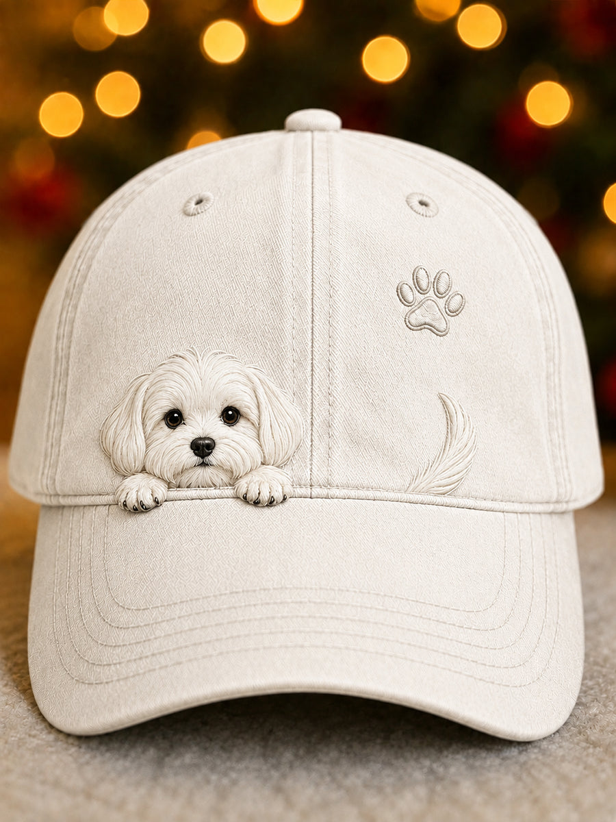 Frontansicht der cremeweißen Kappe mit aufgestickter Hundewelpen-Grafik, Pfotenabdruck und Rute vor weihnachtlichem Lichterhintergrund. 1