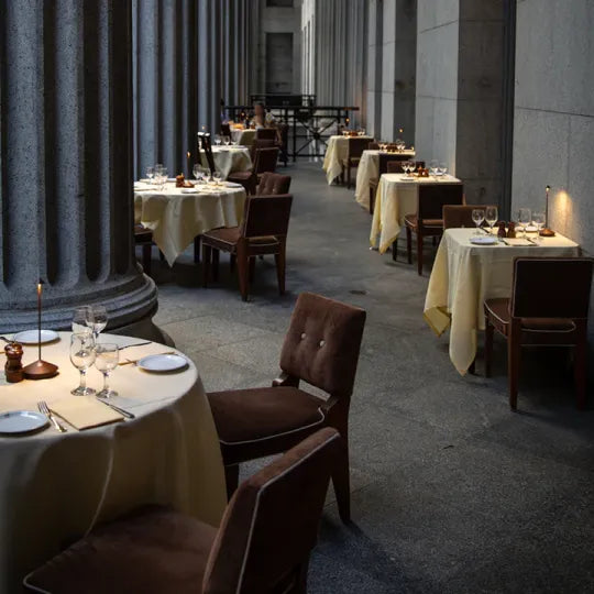 Elegantes Restaurant mit gedeckten Tischen, braunen Stühlen, Kerzenlicht, Säulen, Abendessen.