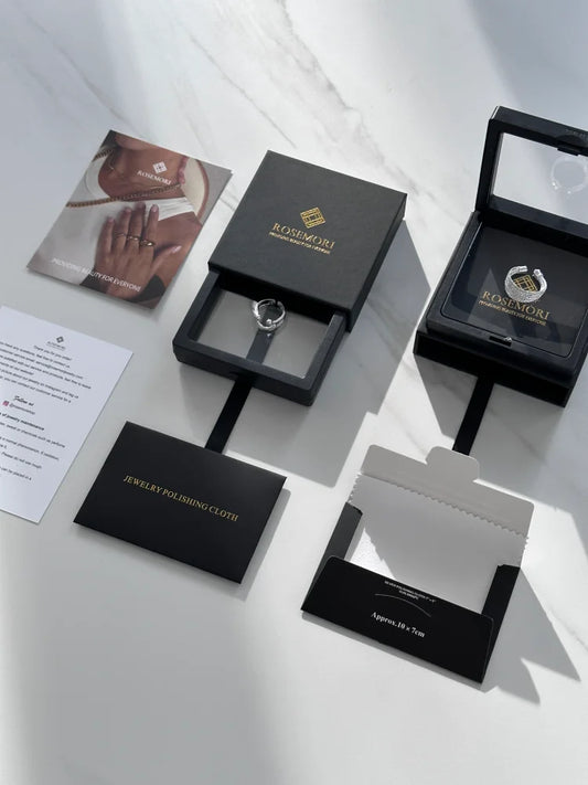 Schwarze Schmuckschachteln mit Ring, Rosimori-Logo, Schmuckpoliertuch, auf weißem Hintergrund.