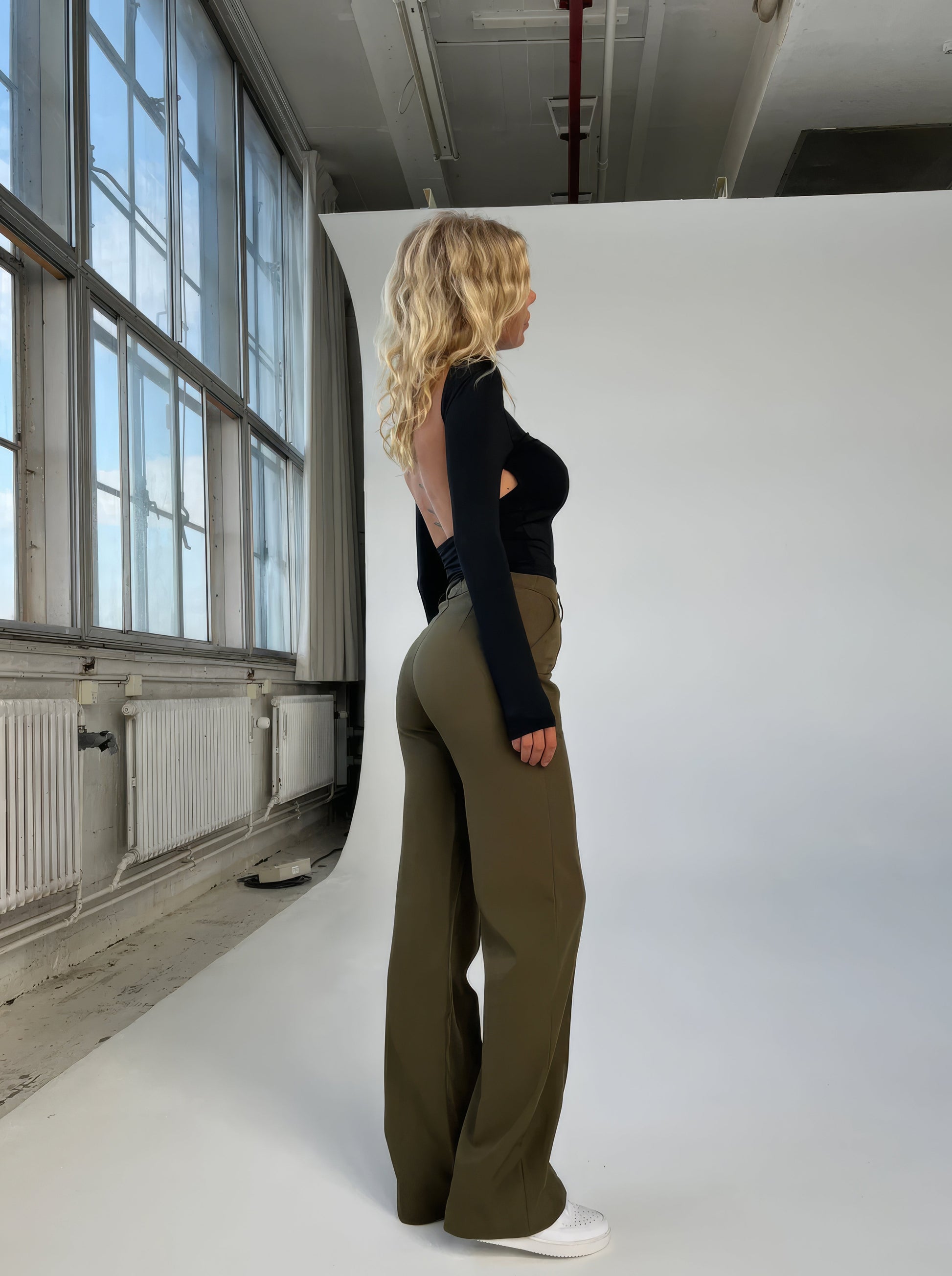 Frau in schwarzem Top und olivgrüner Hose, Studioaufnahme, Modefotografie, Seitenansicht.