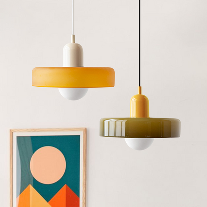 Zwei moderne Pendelleuchten, gelb und olivgrün, aus Glas, vor minimalistischem Hintergrund.