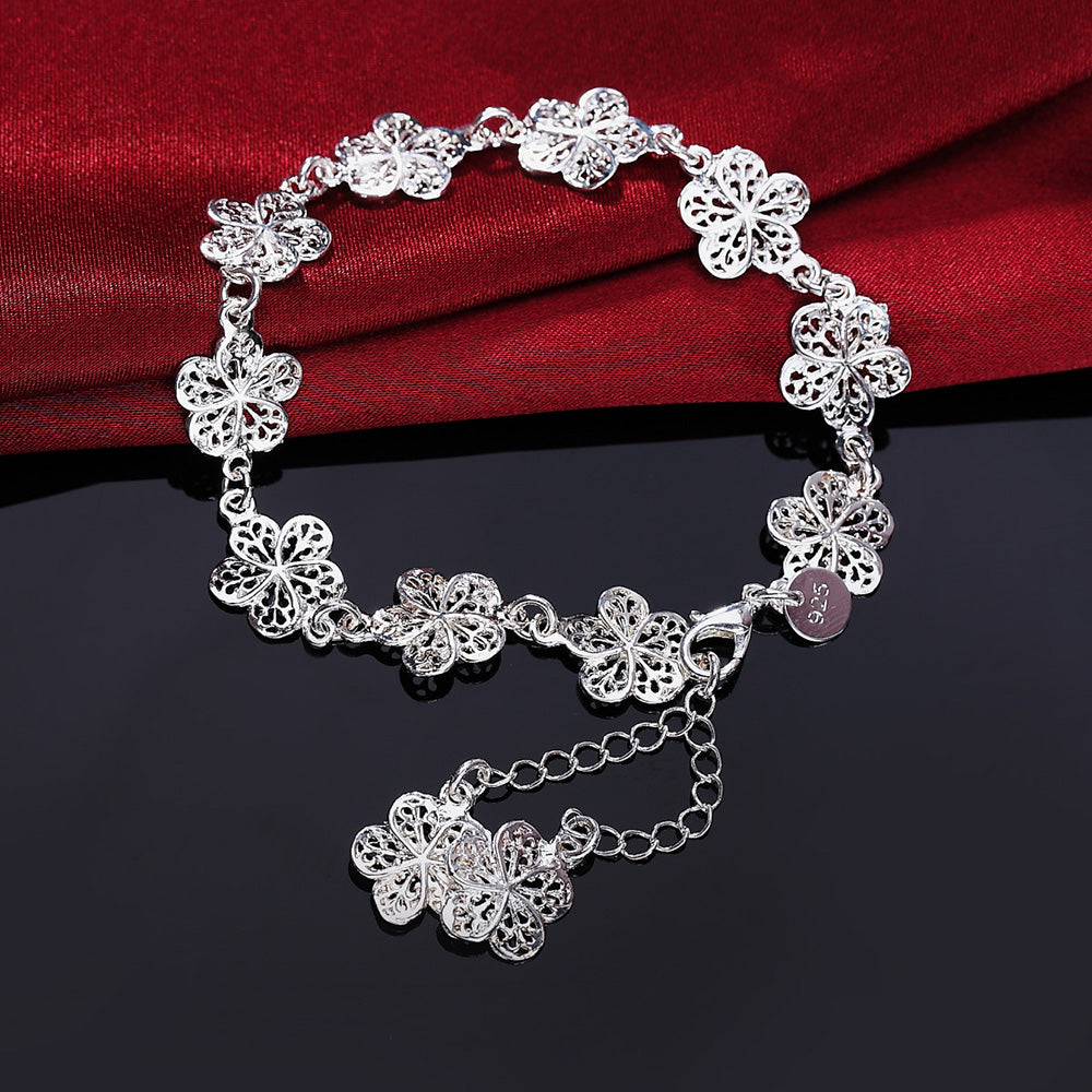 Silbernes Armband mit filigranen Blumenanhängern auf rotem Stoffhintergrund.