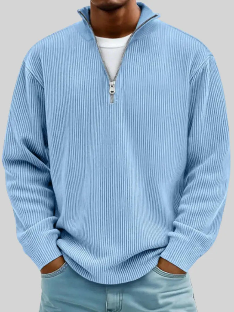 Mann trägt den gerippten Strickpullover in Hellblau mit Stehkragen und Viertelreißverschluss über weißem Shirt, Hände in den Hosentaschen. 1