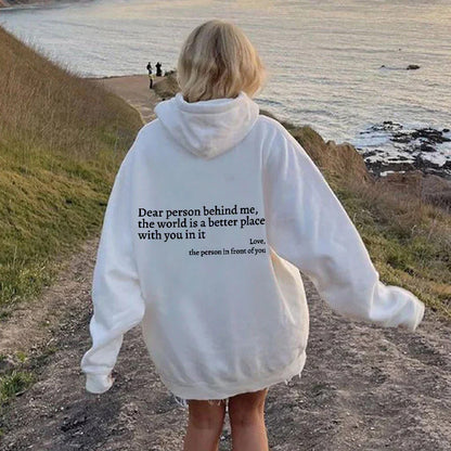 Weiße Oversize-Hoodie mit Rückenaufdruck, Frau am Küstenweg, lässige Mode.