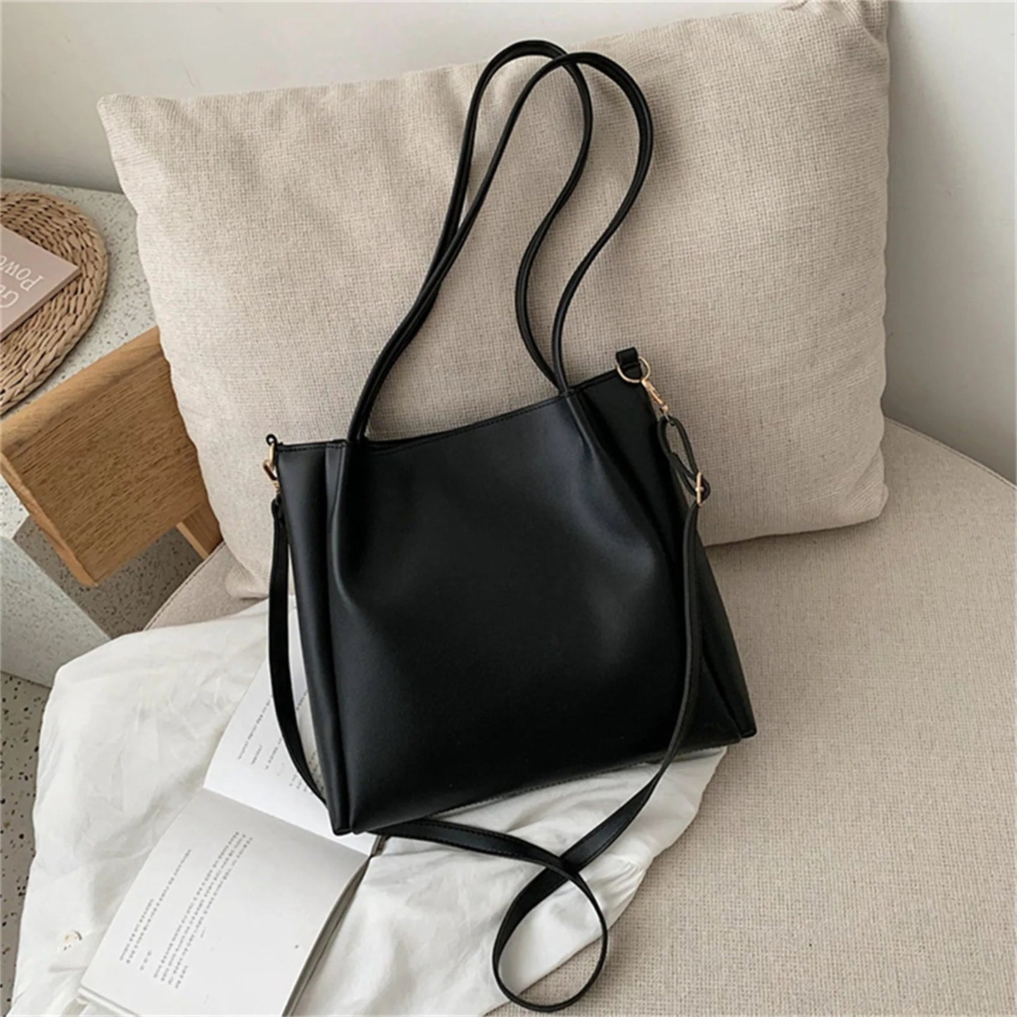 Schwarze Ledertasche auf beigem Sofa, modisch, elegant, Damenhandtasche, minimalistisches Design.