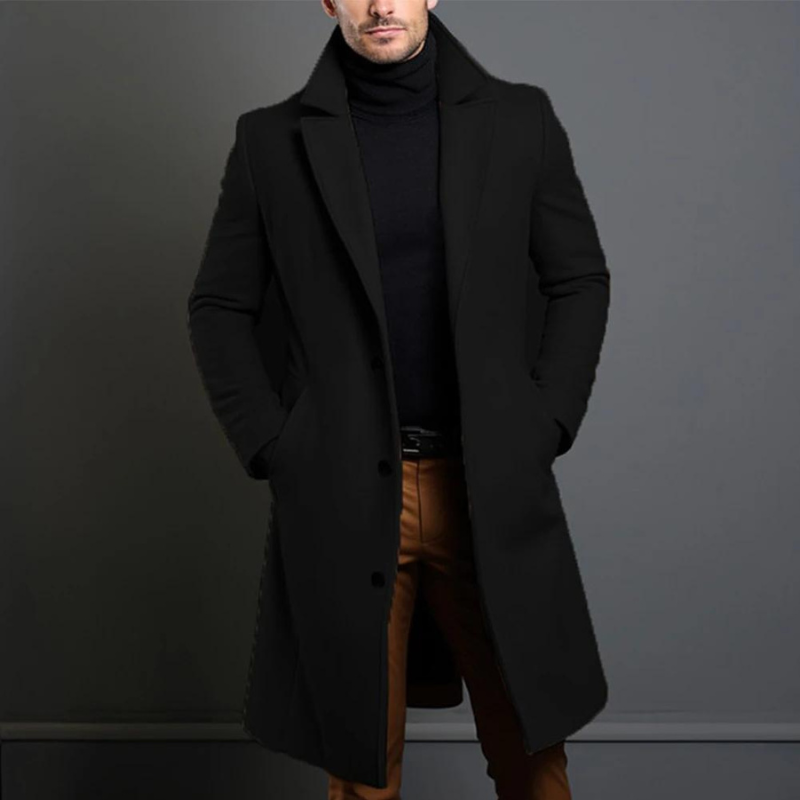 Model trägt den langen einreihigen Mantel in Schwarz mit Reverskragen zu schwarzem Rollkragenpullover und brauner Hose, Hände in den Taschen. 1