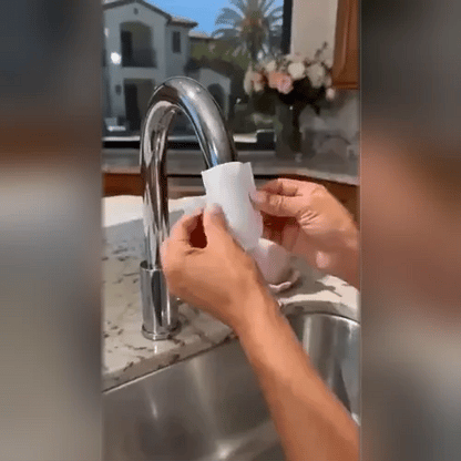 Hände ziehen einen weißen Filterbeutel über den Auslauf eines verchromten Wasserhahns über einer Edelstahlspüle. 2