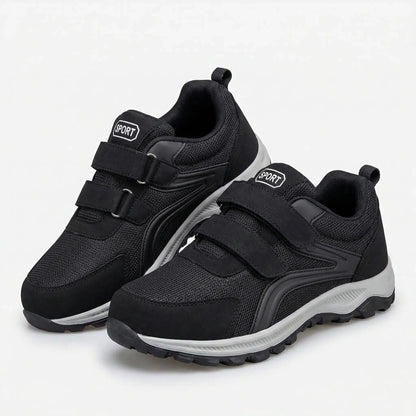 Paar schwarze Klettschuhe mit zwei Riemen und grauer Sohle schräg vor hellem Hintergrund 5
