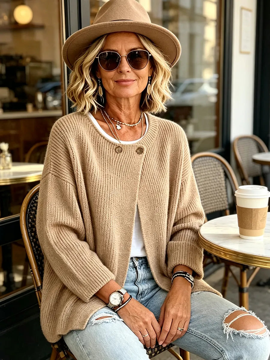 Frau mit Hut und Sonnenbrille trägt die sandfarbene Strickjacke sitzend vor einem Café, daneben ein Kaffeebecher 5