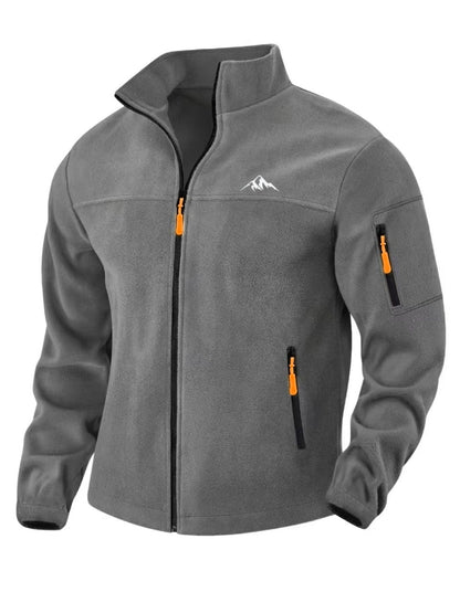 Mittelgraue Fleecejacke von vorn mit Stehkragen, schwarzem Reißverschluss, orangefarbenen Zügen, Ärmeltasche und weißem Bergmotiv auf der Brust. 5