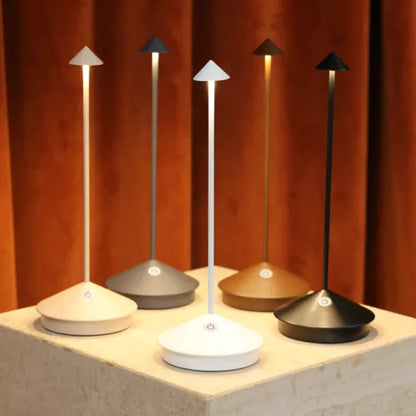 Fünf moderne LED-Tischlampen in verschiedenen Farben auf einem Podest vor braunem Vorhang.