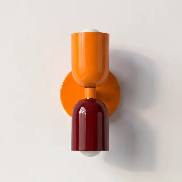 Wandleuchte mit orangefarbenem oberem Schirm und orangefarbener Wandplatte, der untere Schirm ist glänzend dunkelrot, vor heller Wand. 25