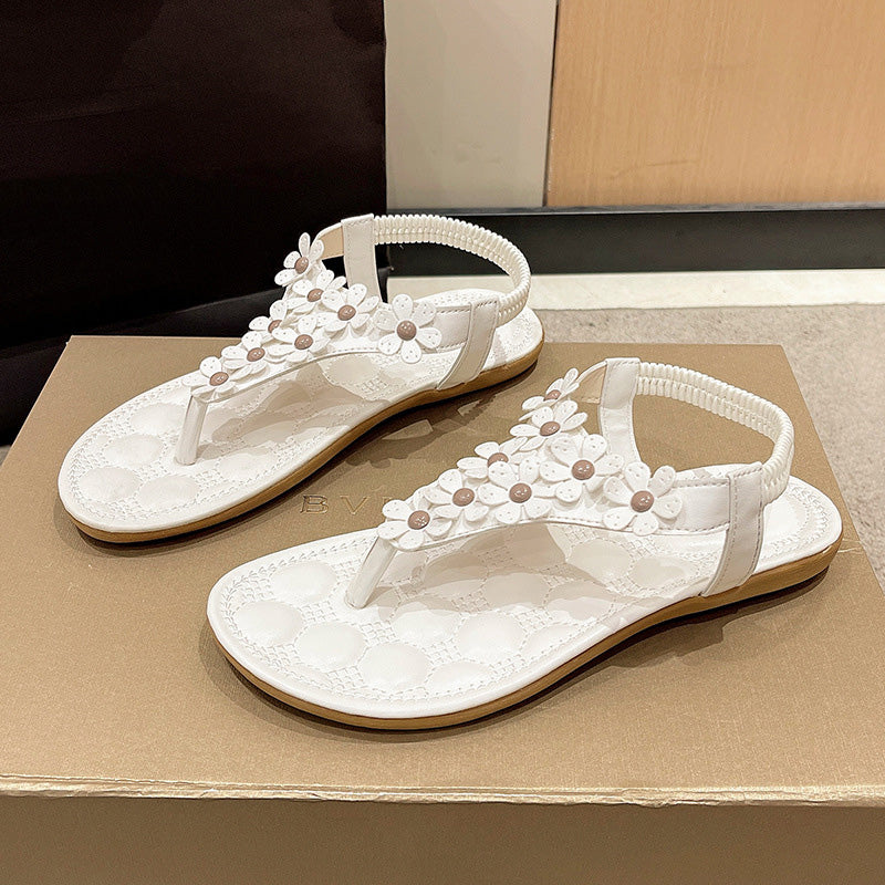 Weiße Damensandalen mit Blumenverzierung, flach, bequem, Sommermode, auf Karton.