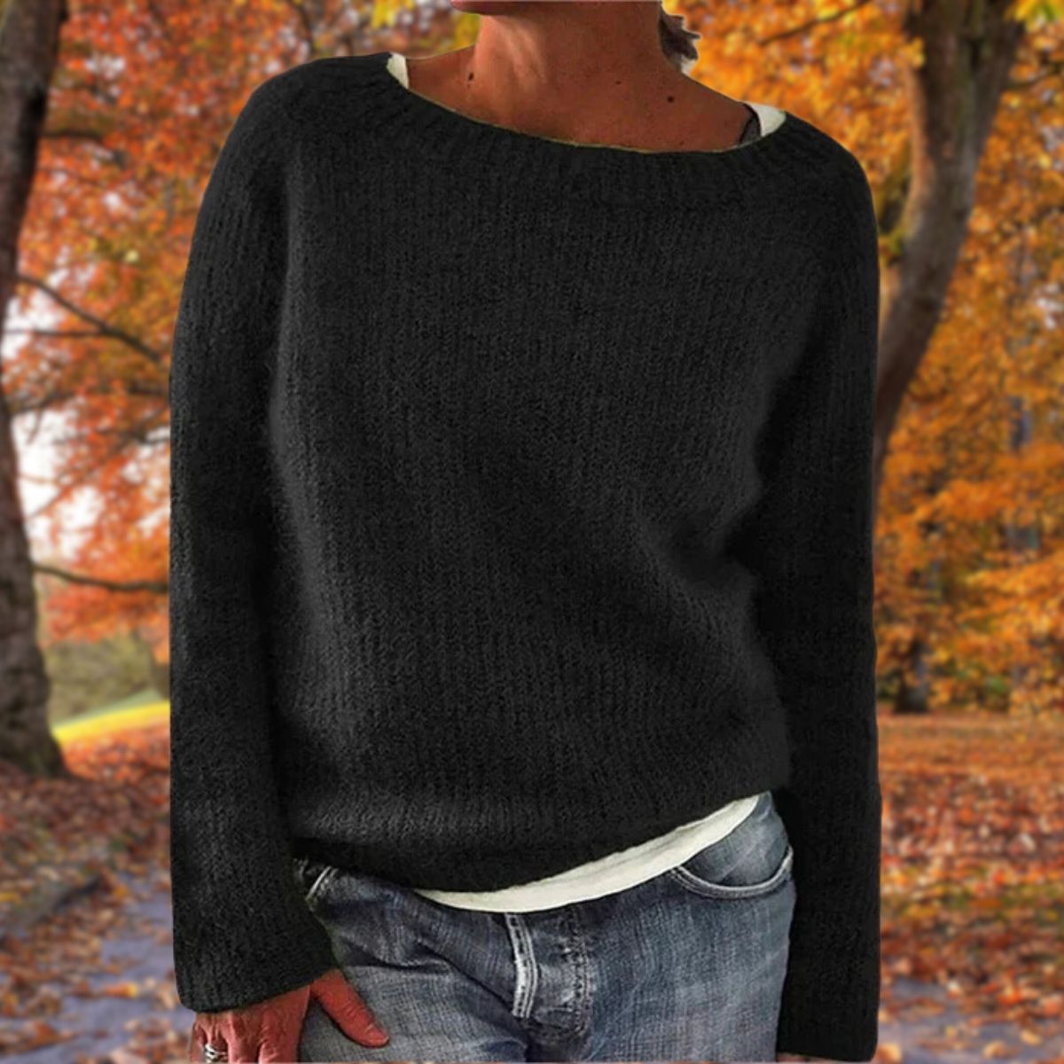 Schwarzer Strickpullover mit Rundhalsausschnitt, getragen über einem weißen Shirt und Jeans vor buntem Herbstlaub. 2