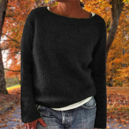 Schwarzer Strickpullover mit Rundhalsausschnitt, getragen über einem weißen Shirt und Jeans vor buntem Herbstlaub. 2
