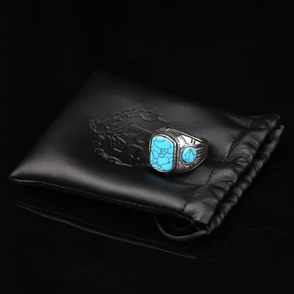 Silberner Herrenring mit blauem Türkis-Stein auf schwarzem Lederbeutel, Schmuckaccessoire.