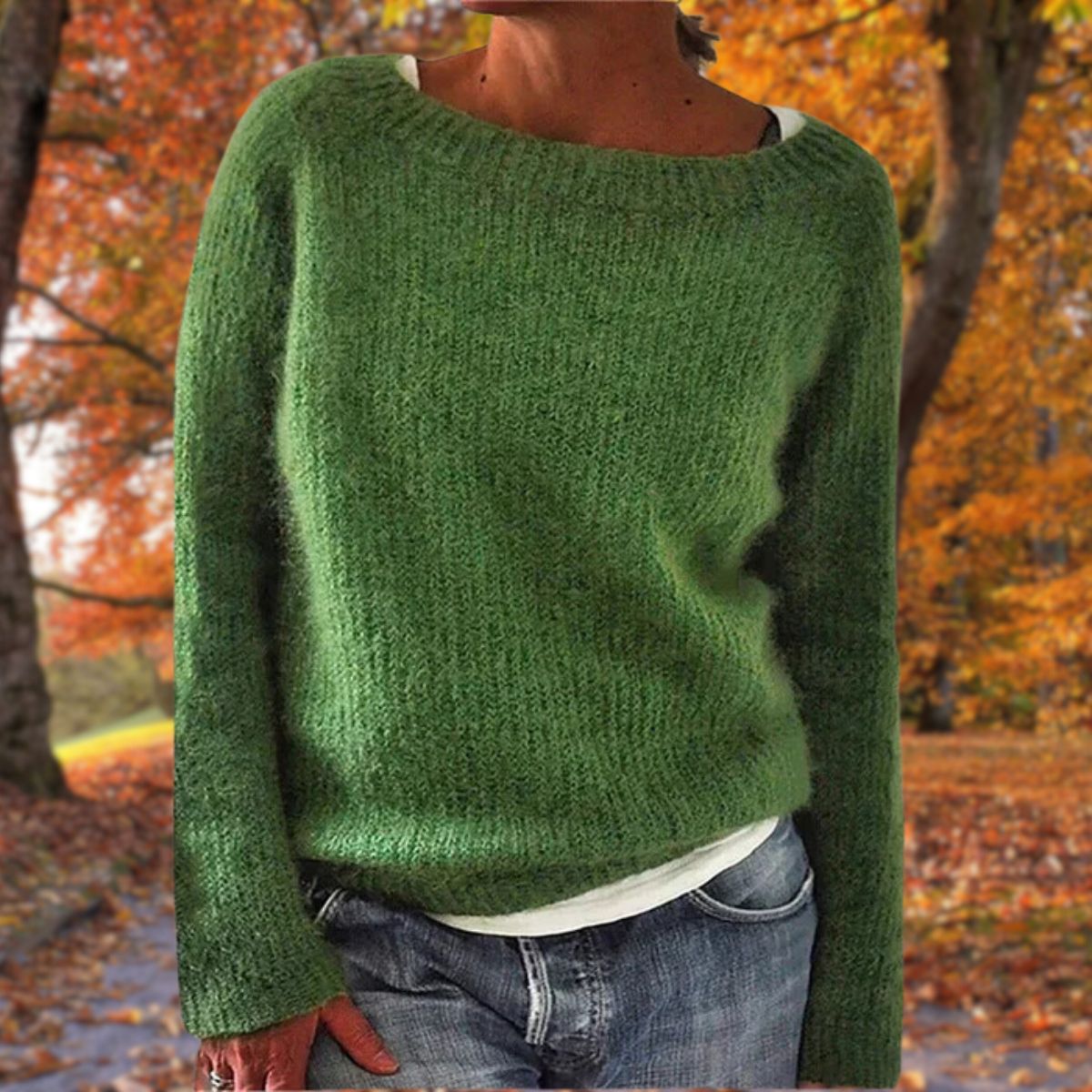 Grüner Strickpullover mit flauschiger Oberfläche, getragen zu Jeans und weißem Unterziehshirt vor orangefarbenem Herbstlaub. 5