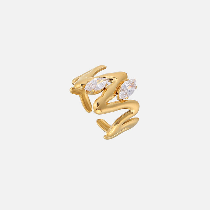 Goldfarbener Ring mit wellenförmig geschwungenem Band und zwei spitzovalen, klaren Steinen, schräg von oben vor hellem Hintergrund fotografiert. 1