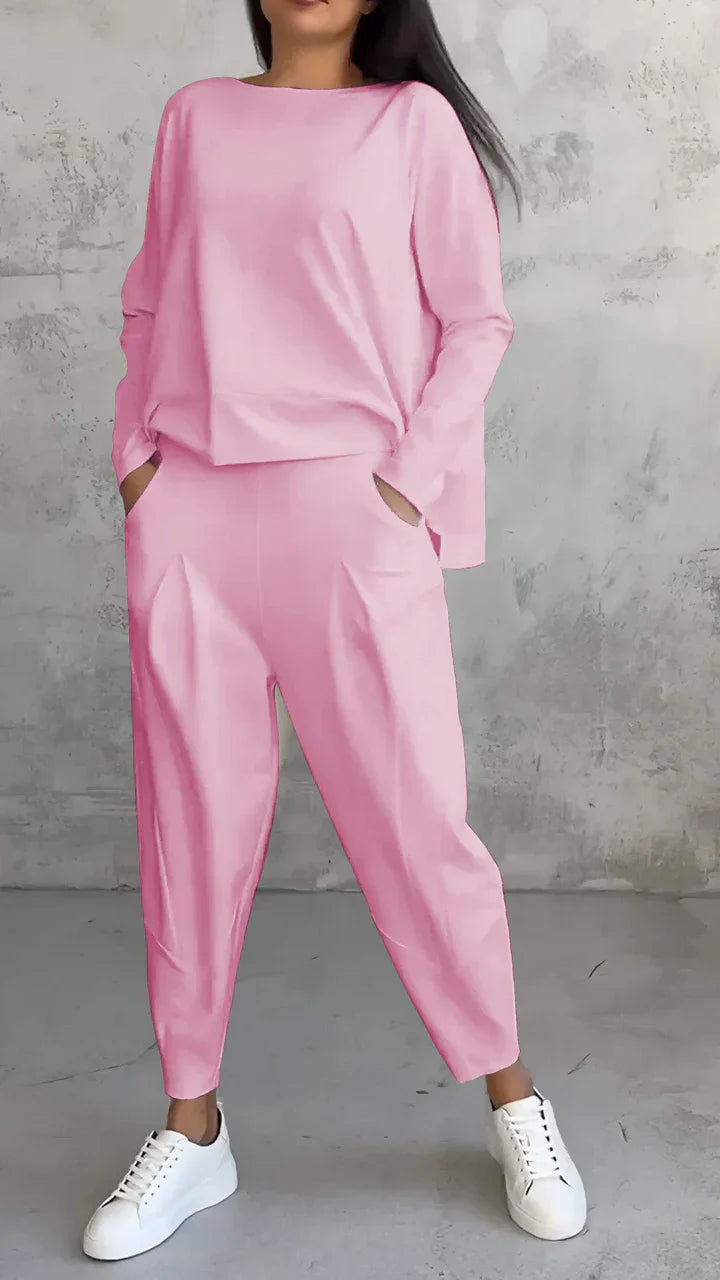 Frau in rosa Freizeitanzug mit weißen Sneakers vor grauer Wand.