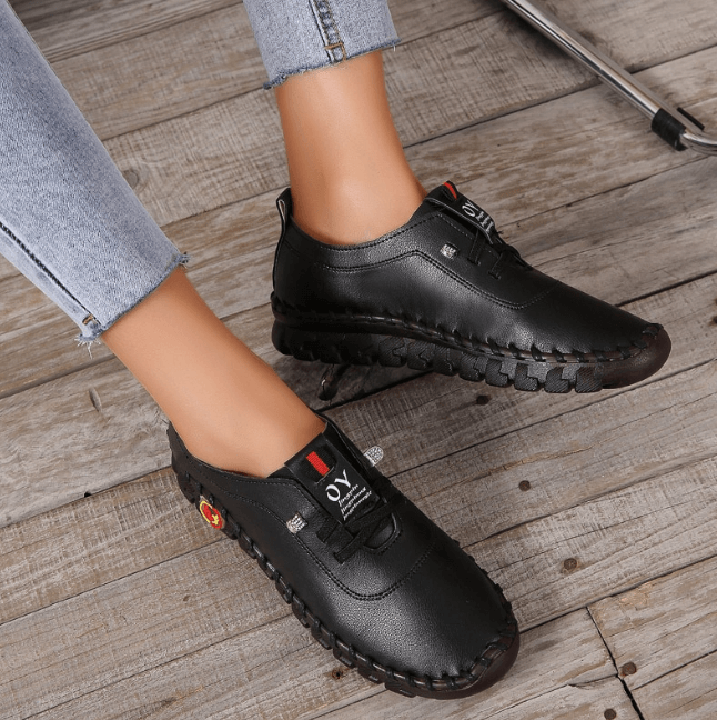 Schwarze Damen-Ledersneaker, handgefertigt, lässig, bequem, auf Holzboden.